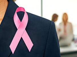 Breast cancer ribbon on a woman's jacket with colleagues in the background