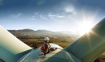 Happy engineer feel success after good work. He standing a top of windmill and looking beautiful sunset landscape